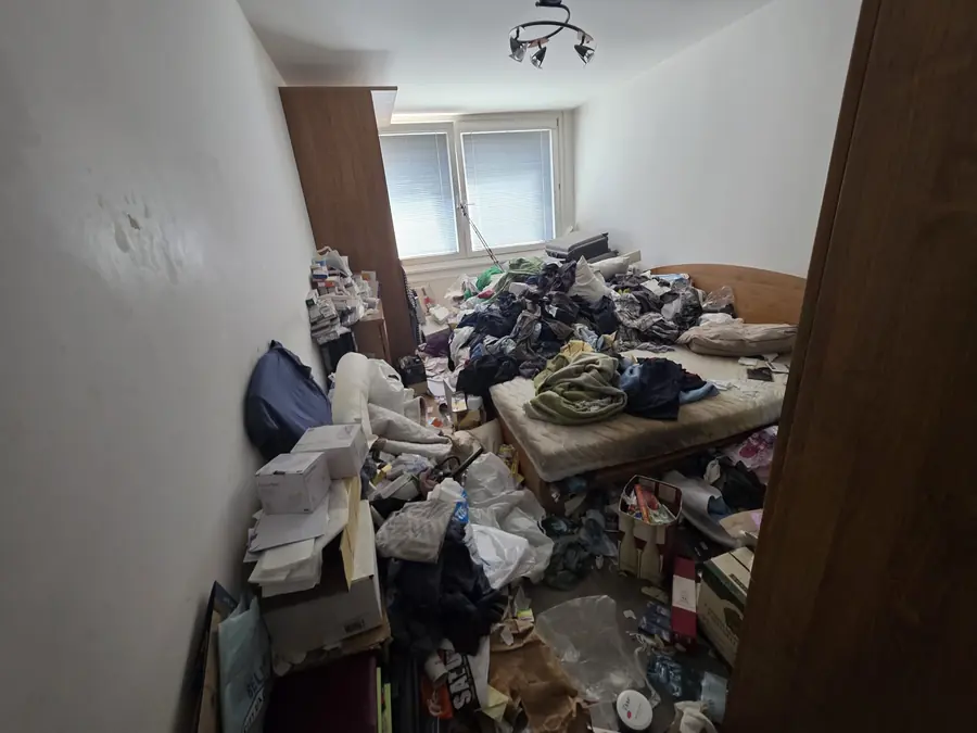 Stark vollgestelltes Schlafzimmer in Linz mit Kleidung auf dem Bett und Kisten am Boden vor einer Privatentrümpelung