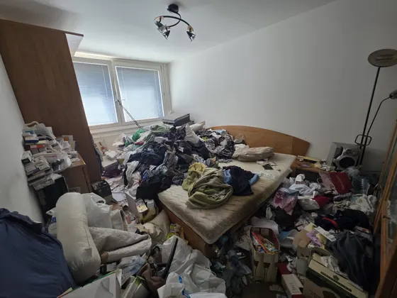 Möbeldemontage und Räumung Linz-Urfahr (4040) – vollgestelltes Schlafzimmer mit Kleiderbergen auf Bett und Boden vor der Räumung